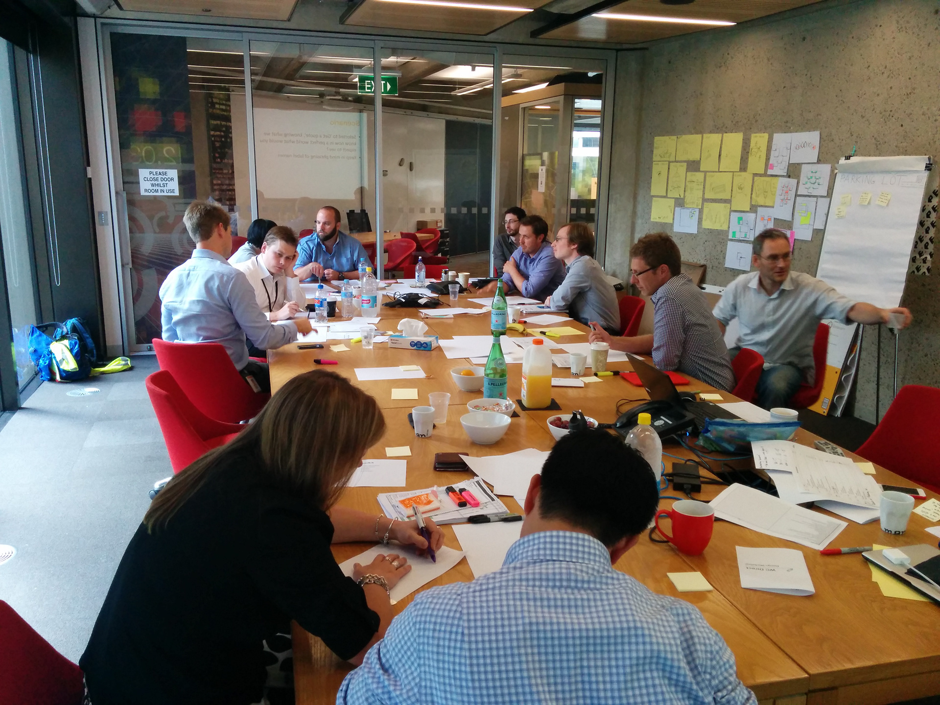 Delivery team collaborating in a workshop session around a large table covered in sketches and sticky notes